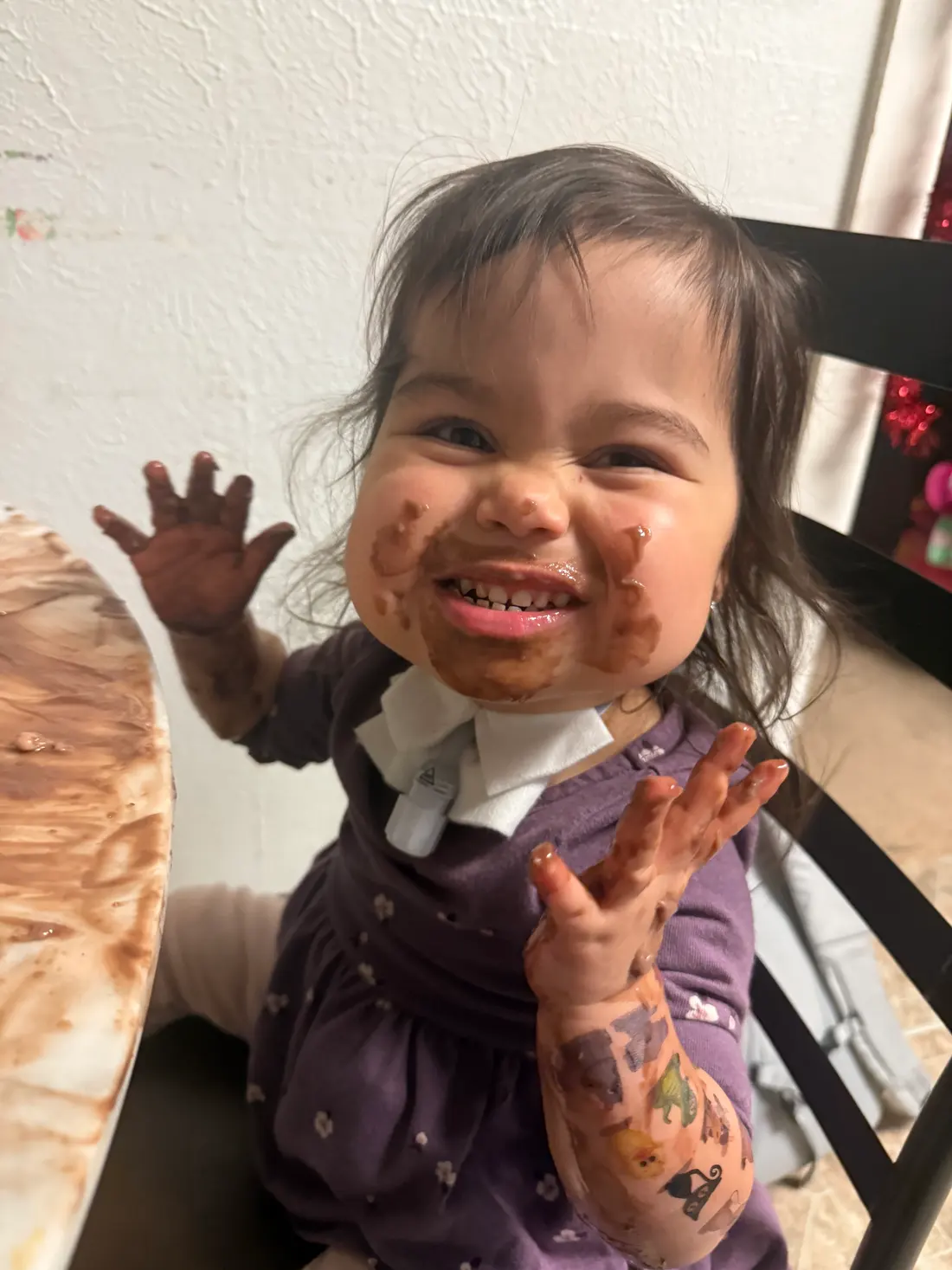 A toddler laughs with both hands raised, face and arms covered in pudding.